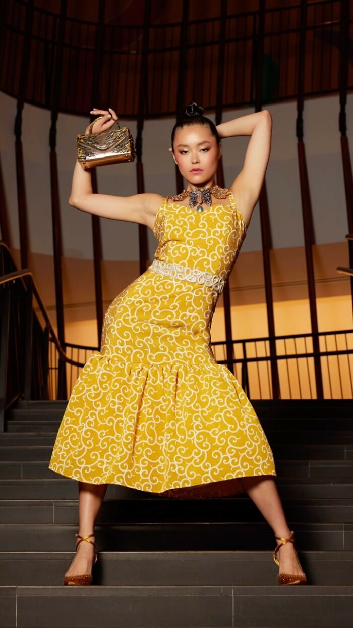 Fashion prodigy design: model in an ornate yellow dress poses confidently on a staircase, showcasing youthful creativity.