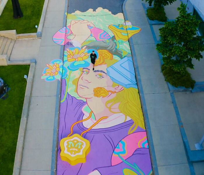 Colorful mural by a Montréal artist on a street, depicting a person with flowers, viewed from above.