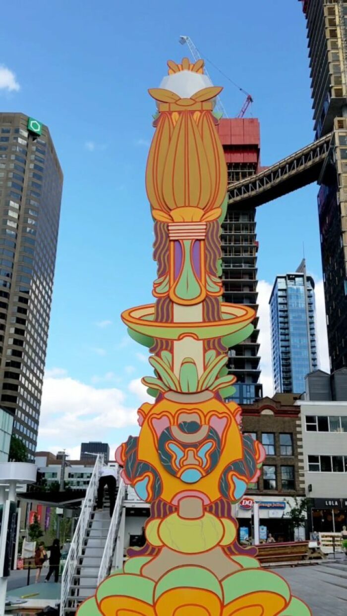 Colorful mural by Montréal artist against city skyscrapers.