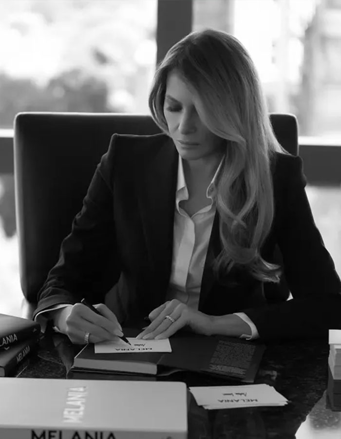 A woman in formal attire writing at a desk, surrounded by books, in a black-and-white setting, related to freelance magician.