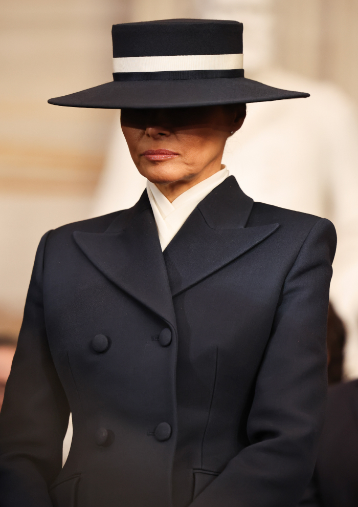 Woman in a dark coat and wide-brimmed hat at a presidential inauguration, showcasing controversial outfit style.