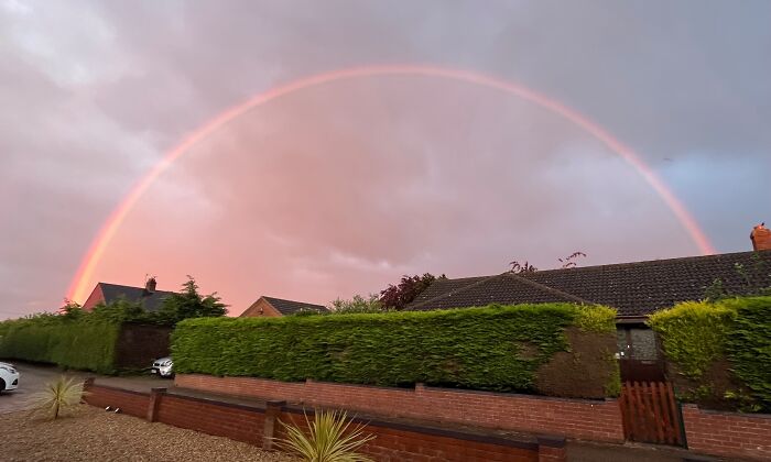 Vibrant rainbow arches over suburban homes, showcasing a stunning natural phenomenon against a colorful sky.