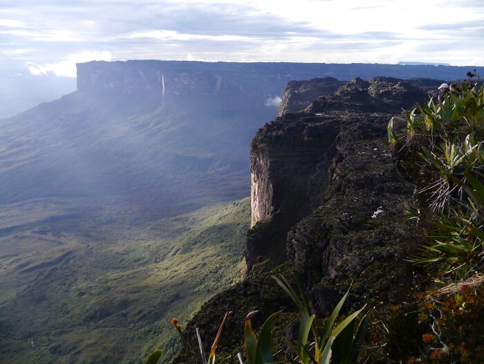 Stunning natural phenomena with a dramatic cliff and lush landscape under cloudy skies.