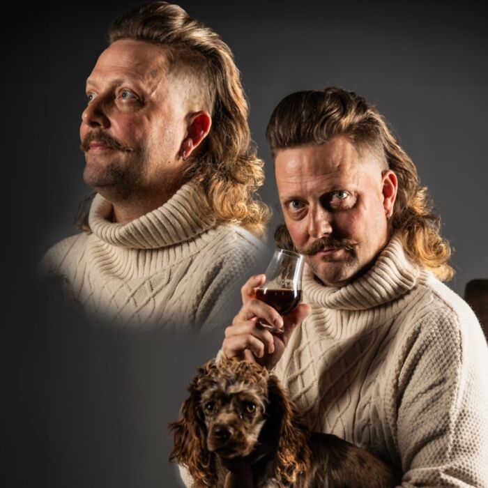 Man with a stylish mullet, wearing a cream sweater, holding a drink and a dog, showcasing a trendy hairstyle.