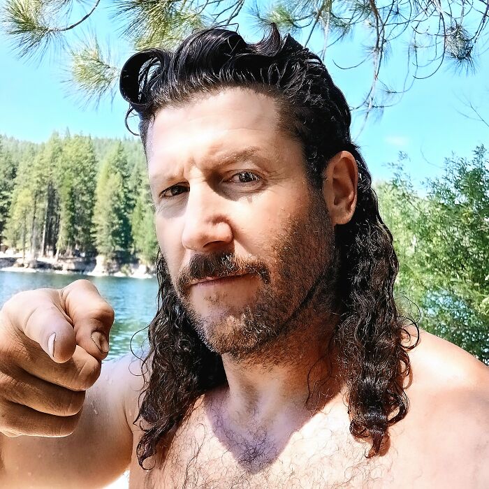 Man outdoors with a mullet hairstyle by a lake, showcasing a trendy 2024 hairdo.