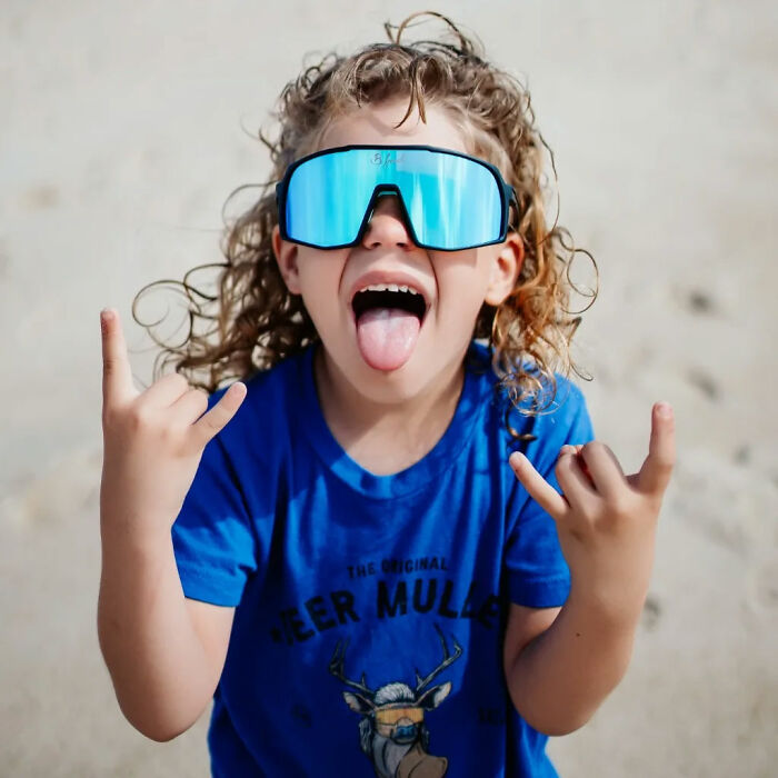 Child in a blue shirt and sunglasses posing playfully, showcasing mullet hairdo.