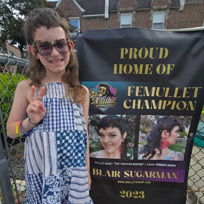 Child posing with mullet championship banner, showcasing trendy mullet hairstyle.