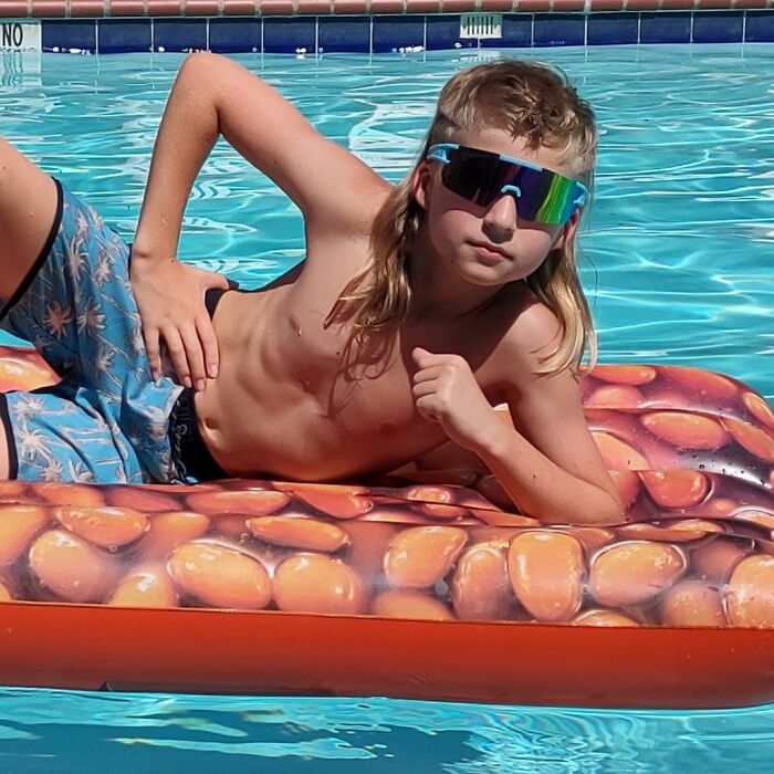 Child with mullet hairstyle relaxing on a pool float, wearing sunglasses, epitomizing trendy 2024 hairdos.