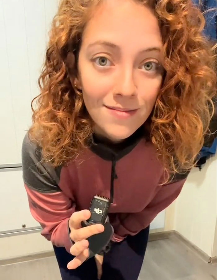 Woman with curly hair holding a device, sharing a Norwegian secret of staying warm.