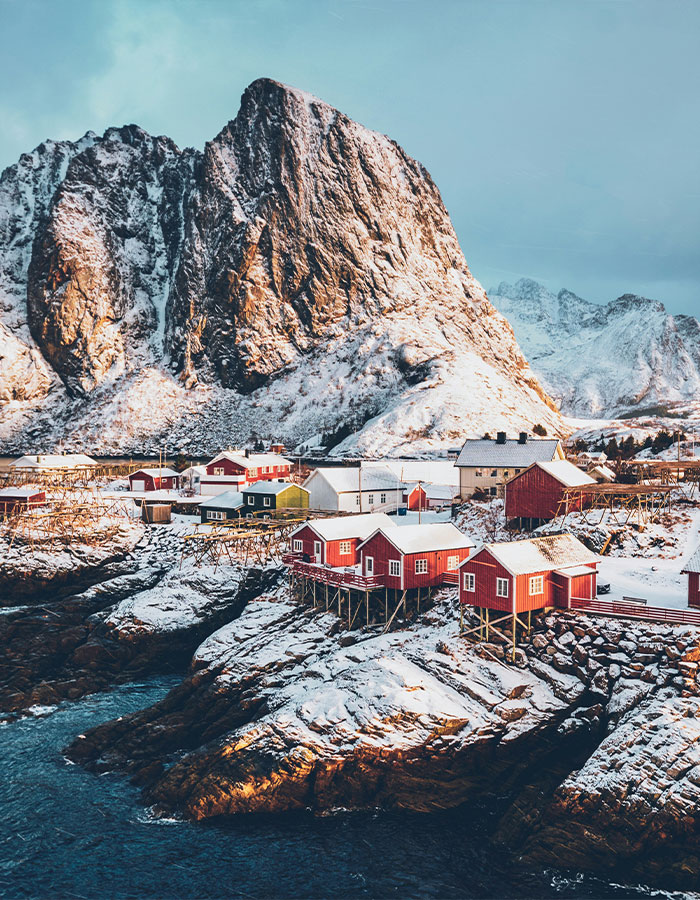 Snowy Norwegian village with colorful houses and dramatic cliffs, illustrating a secret to never feeling cold.