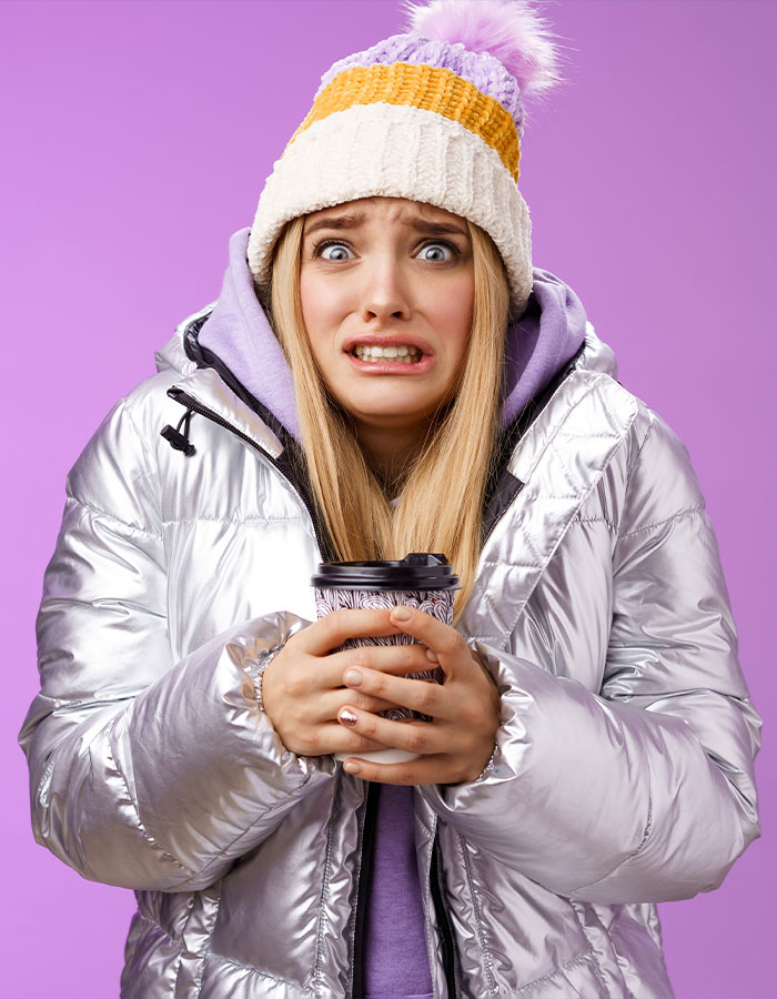 Woman in a silver jacket and colorful hat holding a coffee cup, illustrating a debate on staying warm in cold weather.