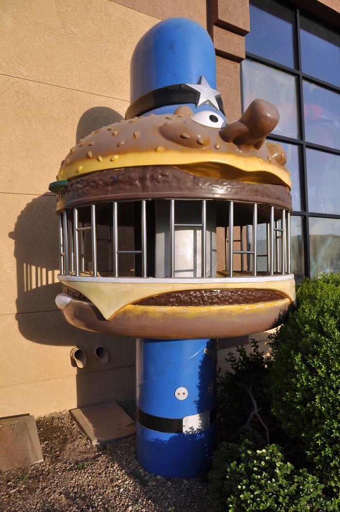 80s nostalgia picture of a whimsical, burger-shaped jail prop with bars, set against an outdoor wall.