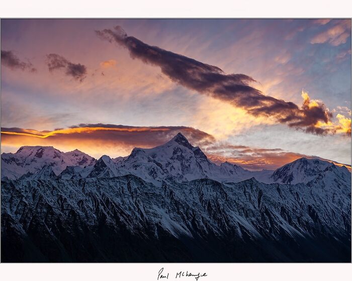 Snow-capped mountains at sunset captured by Paul McKenzie with vibrant sky and dramatic clouds.