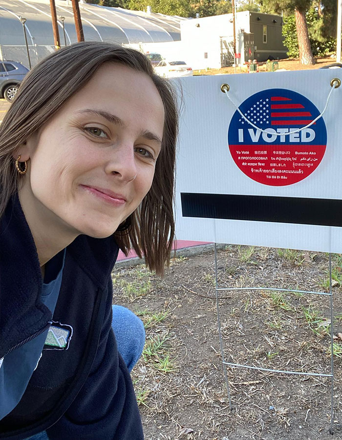 Pauline Chalamet poses with an "I Voted" sign outdoors, smiling and wearing a blue jacket.