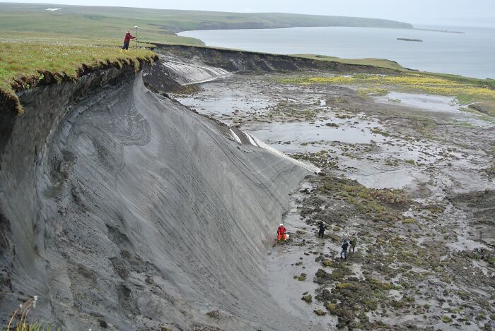 A stunning natural phenomenon featuring a dramatic earth slump with people observing on a grassy cliffside.