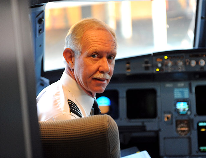 Pilot in a cockpit, discussing fewer ground lights' impact on plane crash theory.