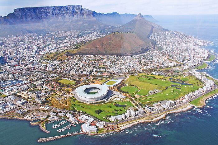 Aerial view of a coastal city featuring a stadium, mountain, and lush green areas highlighting urban landscape.