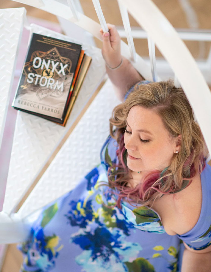 Person sitting on stairs with "Onyx Storm" book beside them, wearing a colorful dress.