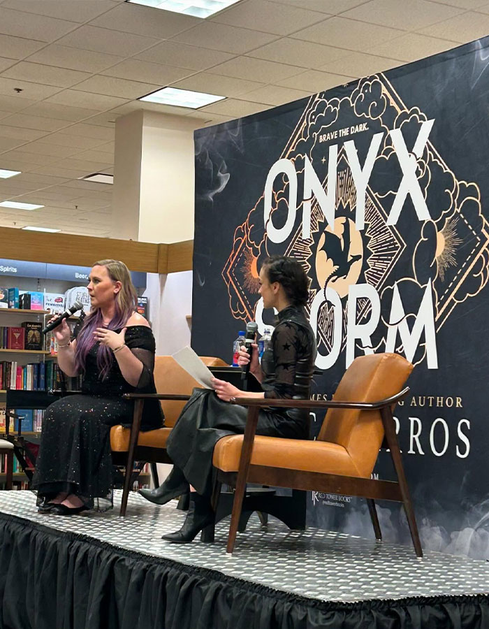 Authors discuss Onyx Storm Craze in a bookstore event, seated on stage with large book poster in the background.