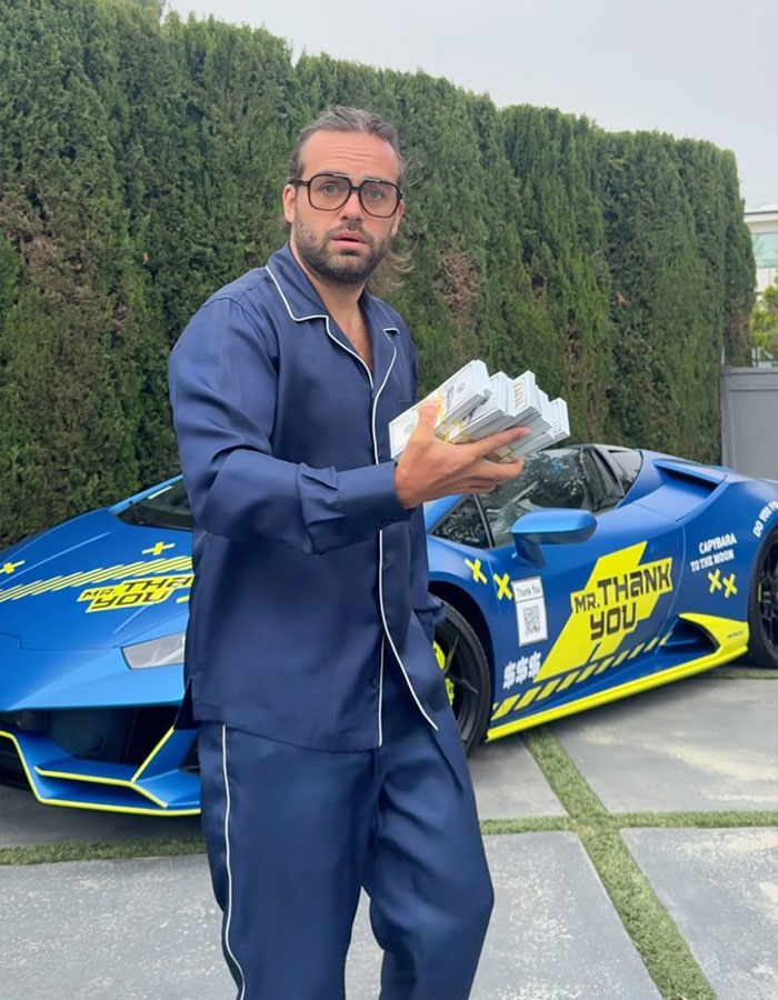 Man in blue pajamas holding items, standing in front of a blue sports car with "Mr. Thank You" on it.