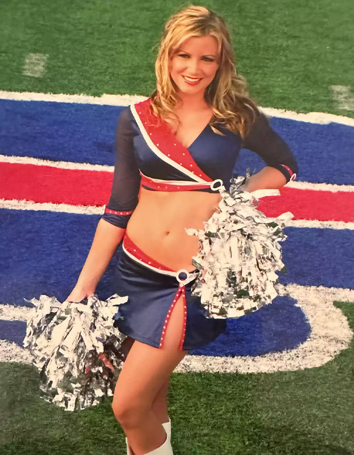 Cheerleader in blue and red uniform holding pom-poms on a football field, Buffalo Bills logo visible.