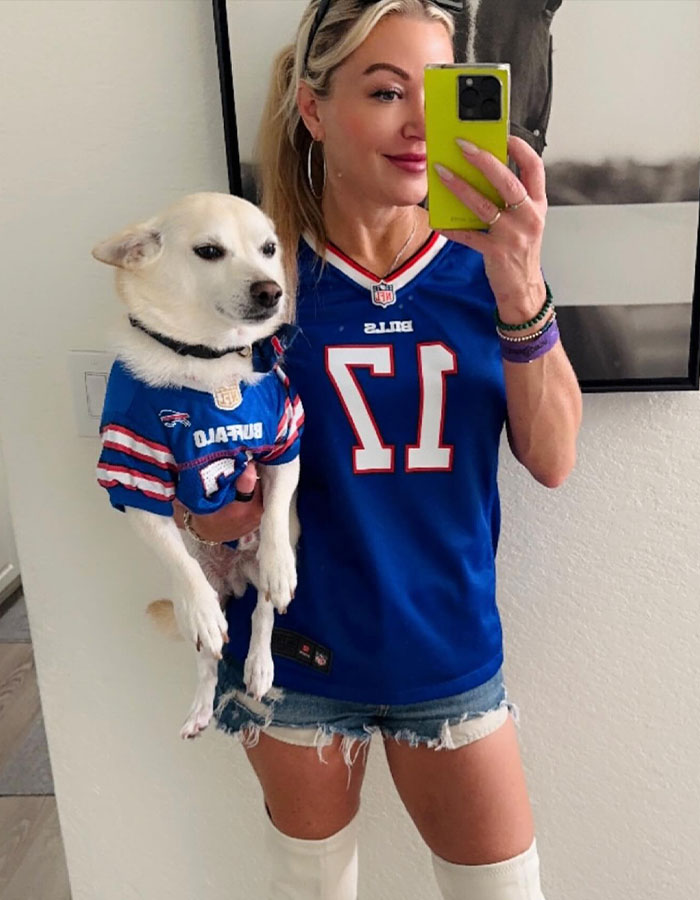 Woman in Buffalo Bills jersey holding dog in matching attire, capturing a selfie.