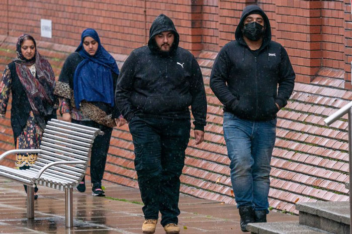 People walking outside a brick building in rainy weather, wearing hooded jackets.