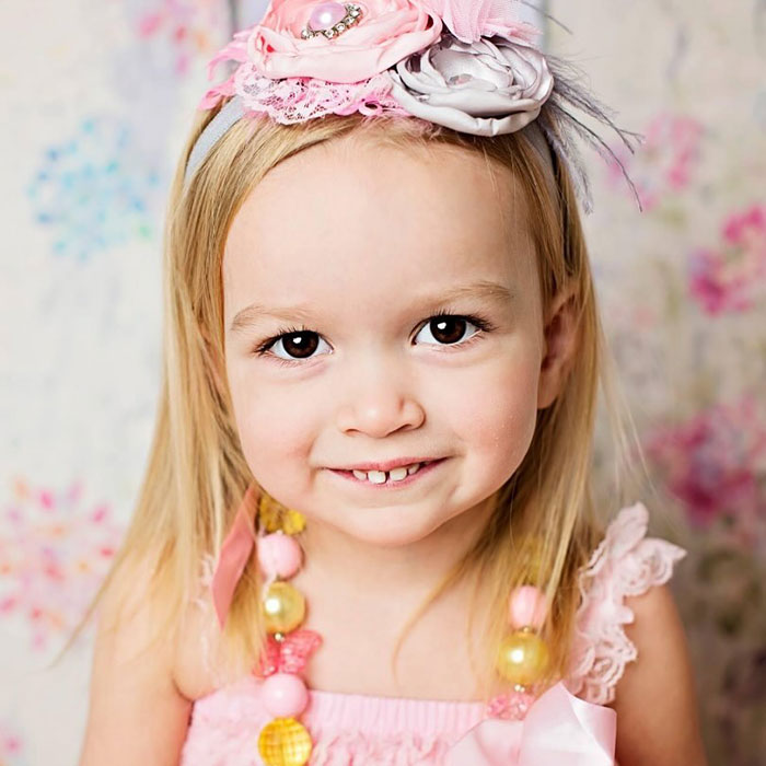 Young girl smiling, wearing a floral headband and colorful necklace, related to the Side-Eyeing Chloe meme.