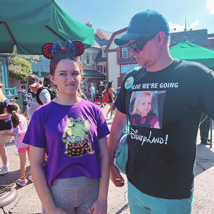 Girl from the viral meme making a funny face at a theme park, accompanied by a man in a shirt referencing the meme.