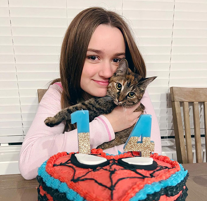 Young girl celebrating her 14th birthday with a cat, featuring a colorful cake in the foreground.