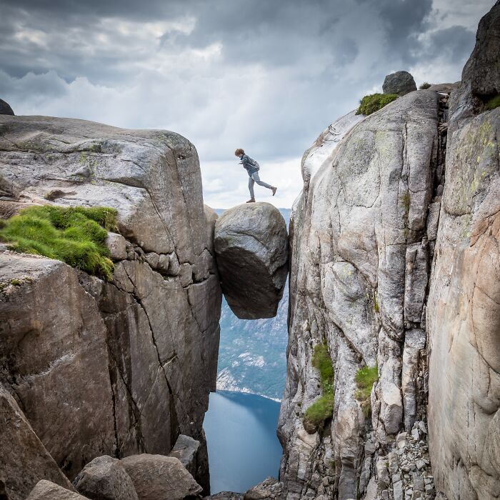 Person standing on a rock wedged between cliffs, showcasing stunning natural phenomena.