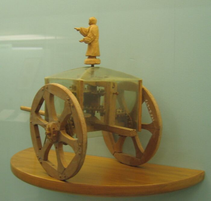 Historical invention model showcasing an ancient automaton with gears and a wooden figure on top, on display.