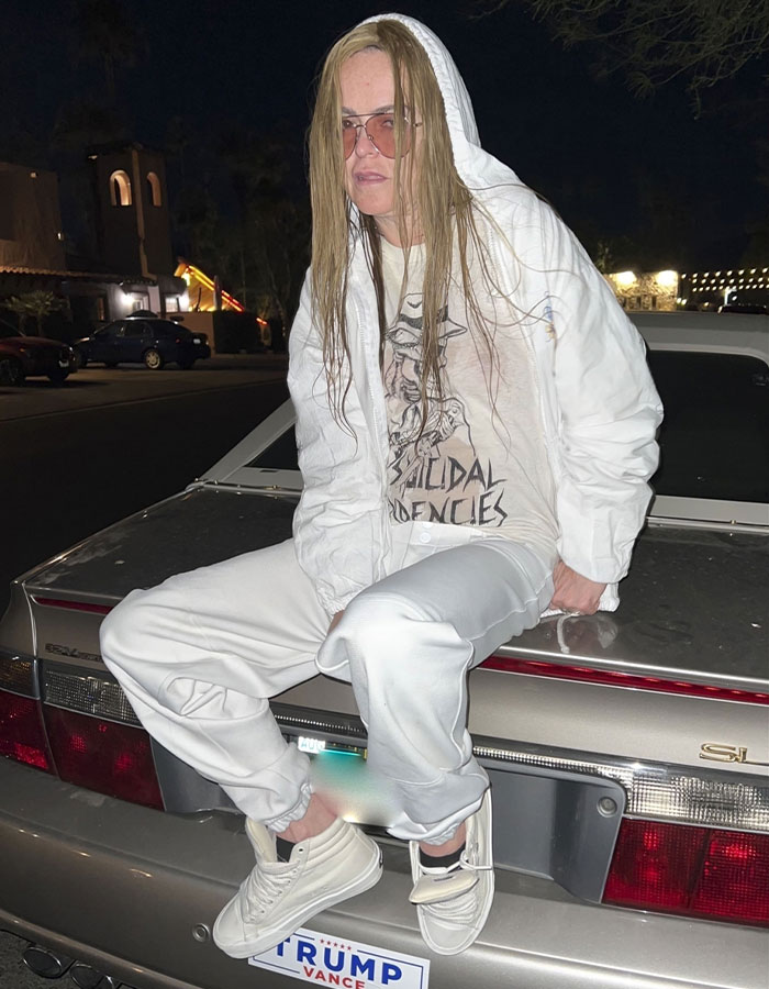 Actress in white outfit and glasses sitting on car, sparking concern.