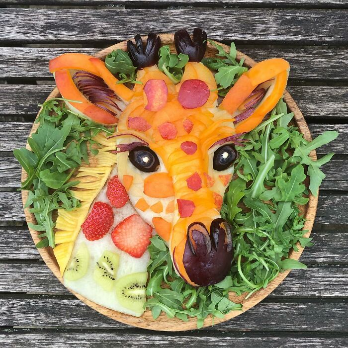 Healthy eating art featuring a giraffe made from fruits and vegetables on a wooden table.