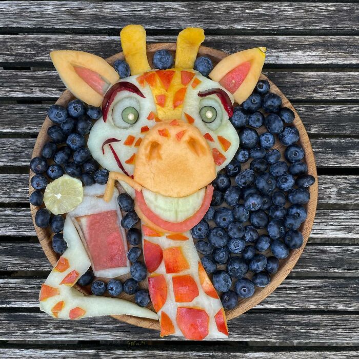 A giraffe made from fruit and berries on a wooden table, showcasing healthy eating as art.