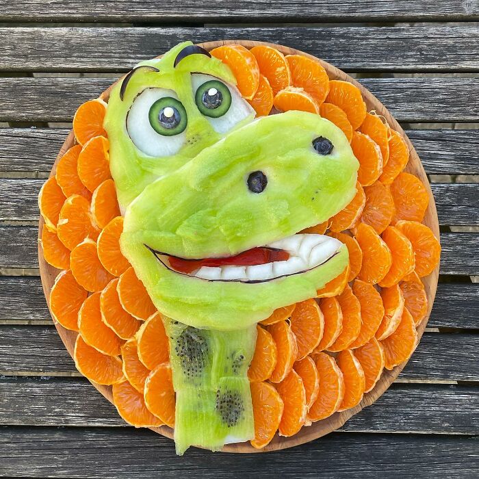 A fruit art piece featuring a dinosaur head made of melon, citrus slices, and kiwi, showcasing healthy eating creativity.