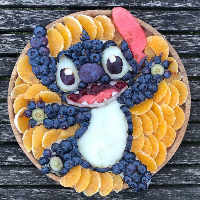 Fruit art depicting a character with blueberries and orange slices on a wooden table.