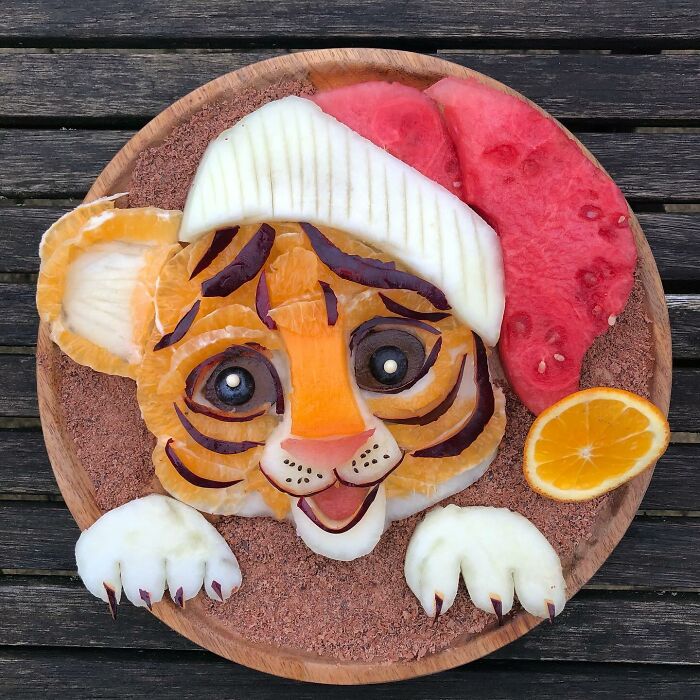 Tiger face made from healthy fruits, showcasing food art on a wooden plate.