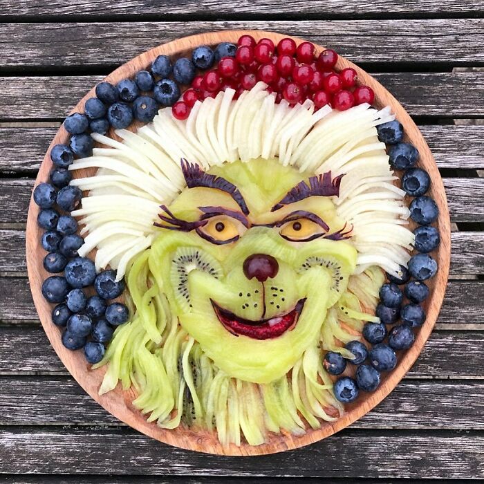 Artistic healthy eating creation made of kiwi, blueberries, and red currants on a wooden plate, resembling a whimsical face.