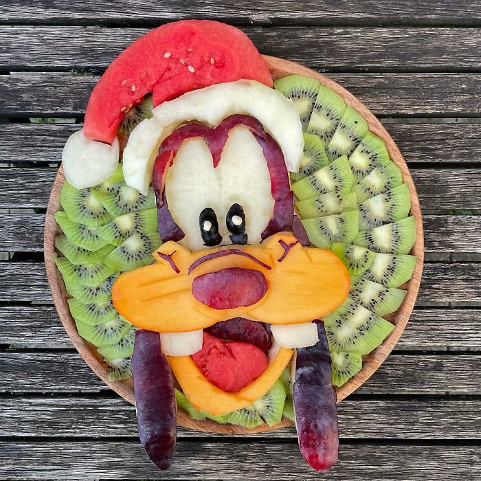 Fruit art on a wooden table, featuring a creative arrangement of kiwi, melon, and berries depicting a cartoon face.