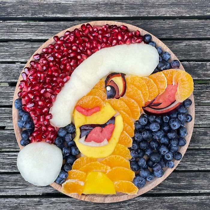 Fruit art depicting a character with a Santa hat, crafted from oranges, blueberries, and pomegranate, showcasing healthy eating art.