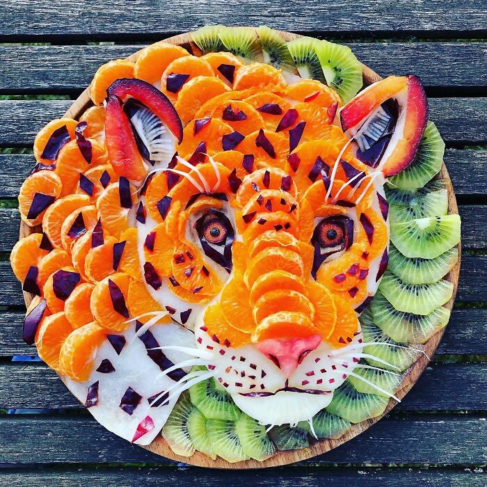 Healthy eating art featuring a tiger face made from citrus, kiwi, and other fruits on a wooden background.