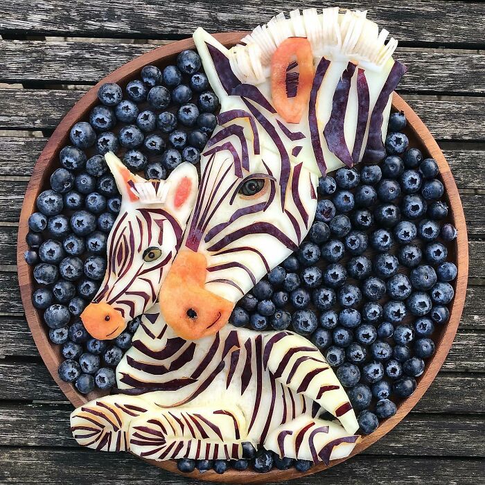 Healthy eating art featuring zebra designs made from fruit, with a background of blueberries on a wooden plate.