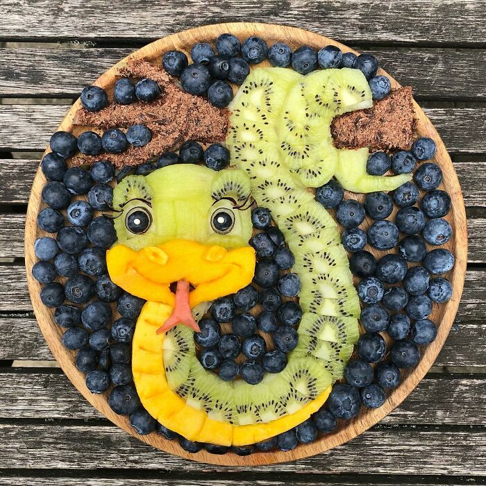 Artistic food arrangement with healthy fruits shaped like a snake, including kiwi, mango, and blueberries.