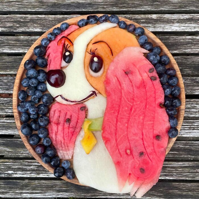 Healthy eating art: a cute dog image made from fruit like watermelon and blueberries on a wooden table.