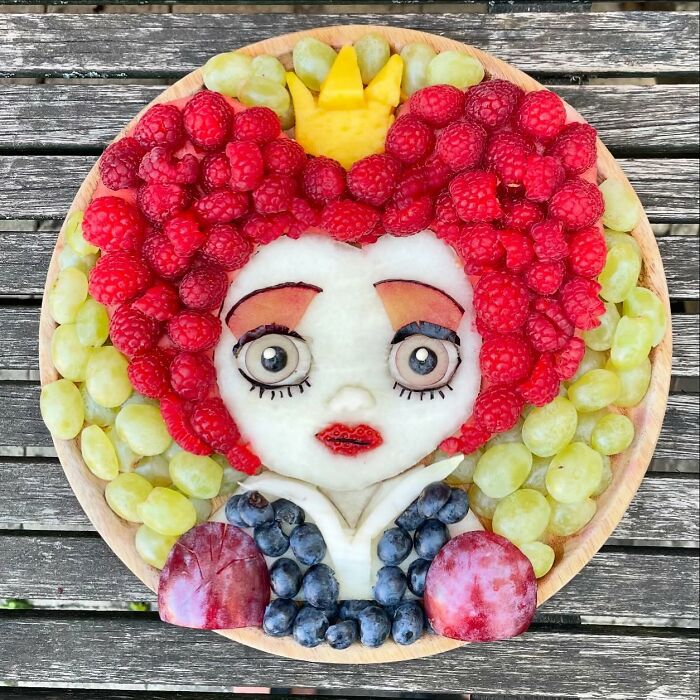 Artistic creation of a face using healthy fruits like raspberries, grapes, and blueberries on a wooden table.