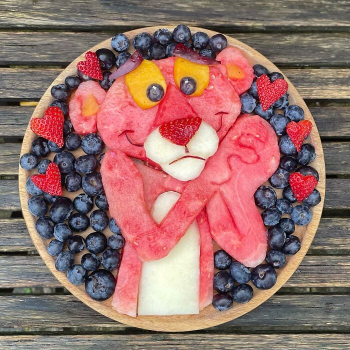 Healthy eating art: Pink character crafted from watermelon, surrounded by blueberries and strawberries on a wooden plate.