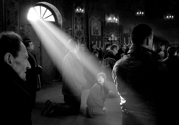 People kneeling in prayer, with a beam of light shining on a child, depicting resilience and beauty in everyday life.