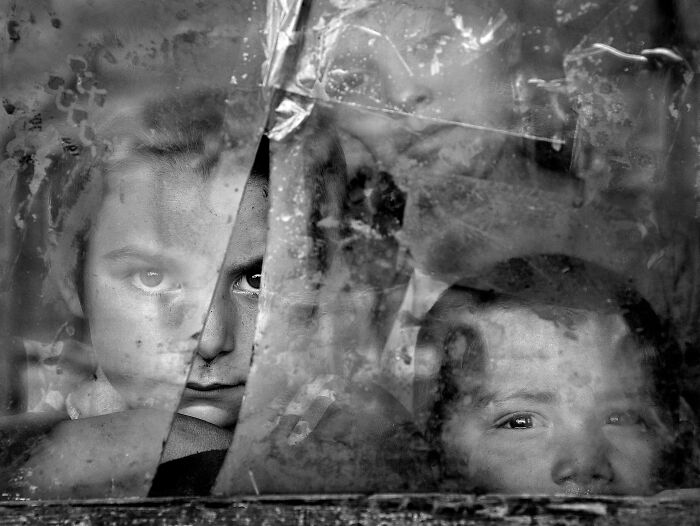 Children looking through a cracked window, captured by Istvan Kerekes, showcasing resilience and beauty of everyday people.