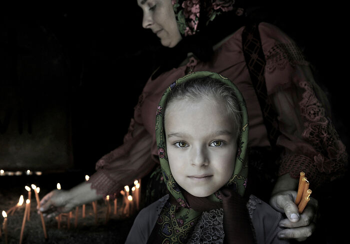 A young girl with a headscarf stands near lit candles, representing resilience and beauty in everyday people.